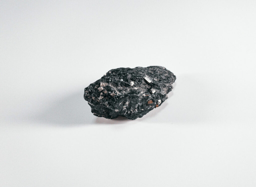 Vue rapprochée d'un morceau brut d'obsidienne noire sur un fond blanc, montrant sa texture rocheuse et ses éclats métalliques ou dorés.