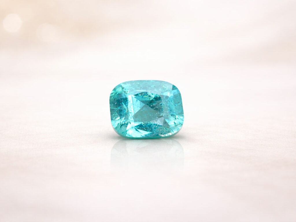 Une tourmaline Paraíba de couleur bleu néon, taillée en forme de coussin, posée sur une surface claire avec un reflet léger